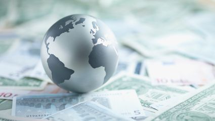 An image of a grayscale globe of Earth sitting upon various paper currencies.