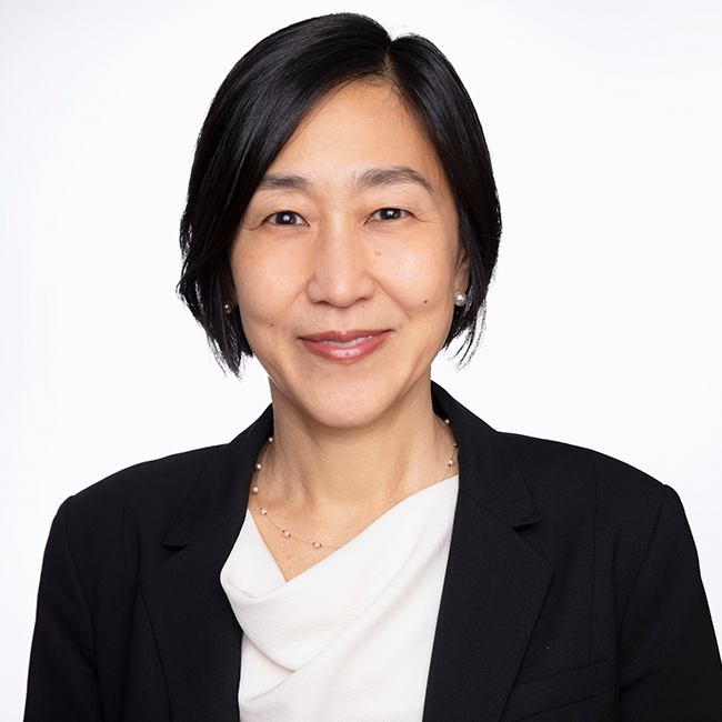 An image of a woman named Alice Chen. She has short black hair, brown eyes, white skin, and is Asian in appearance. She is slightly smiling at the camera against a white background and is wearing a dark blazer over a white shirt.