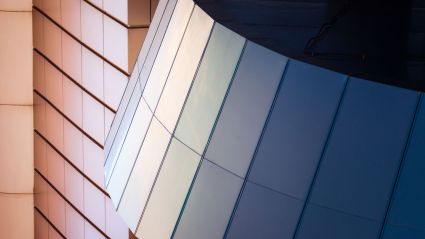 Close-up of a modern building with reflective angled panels in shades of blue and beige.