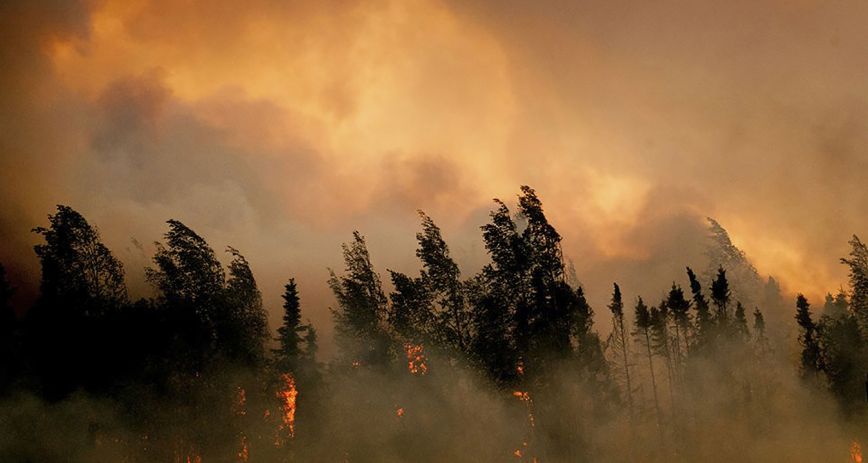 A wildfire burns strongly with wind and smoke