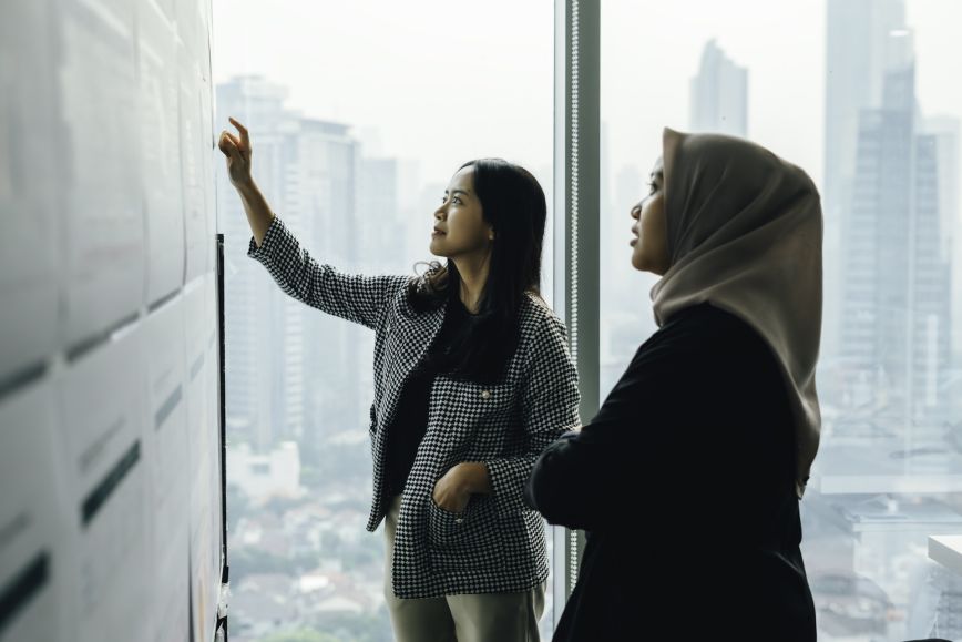 Two women in an office look at set of data on a wall